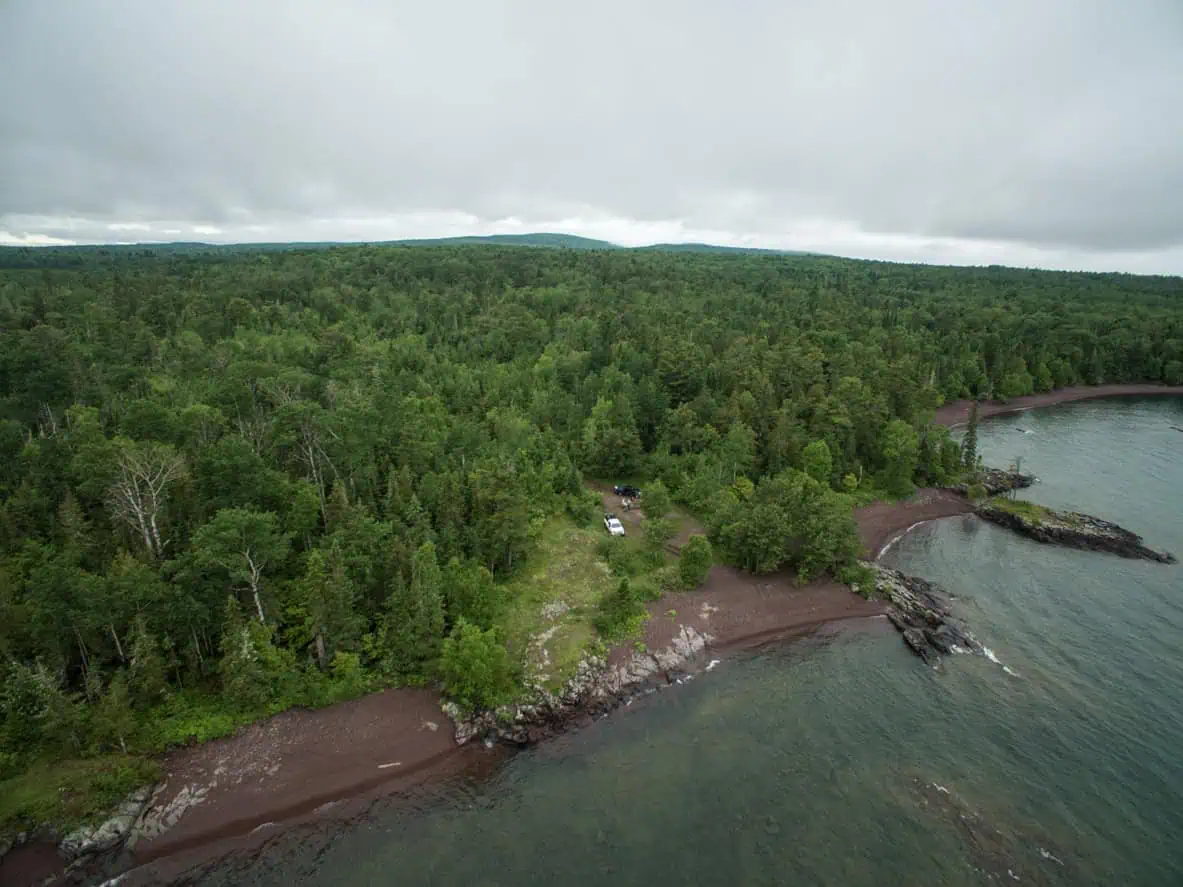 Aerial view of a small clearing with a concrete pad in dense forest on the Lake Superior shoreline at the tip of the Keweenaw Peninsula.