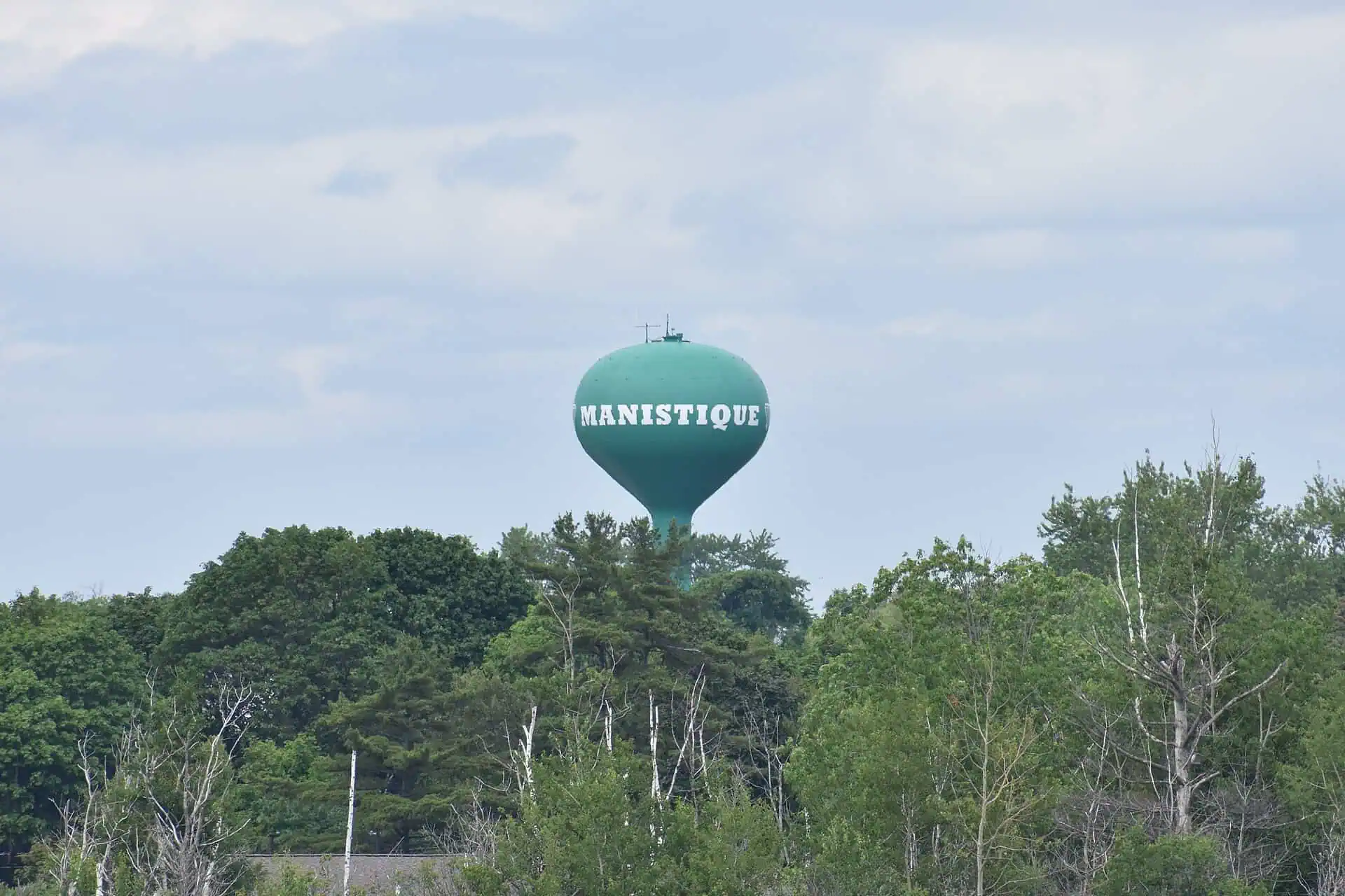 The tall brick Manistique water tower rising above trees in downtown Manistique, Michigan.