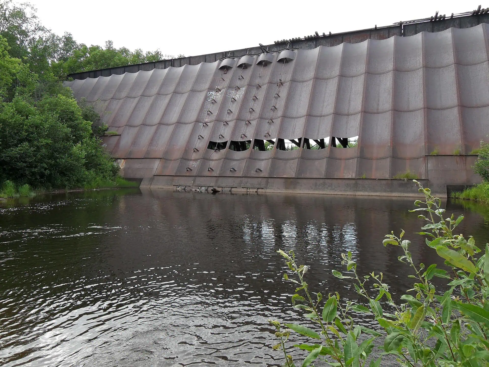 The rusting steel face of the Redridge Steel Dam spanning the Salmon Trout River in Michigan.