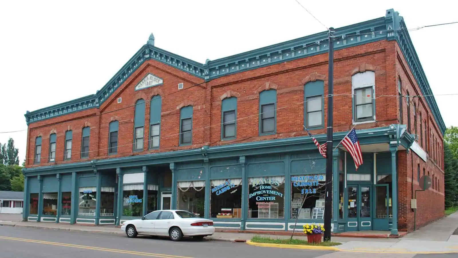A two-story red brick commercial block with green-painted cast-iron storefronts and cornice, "HARRIS BLOCK 1887" lettered on the central pediment, on a small-town main street.