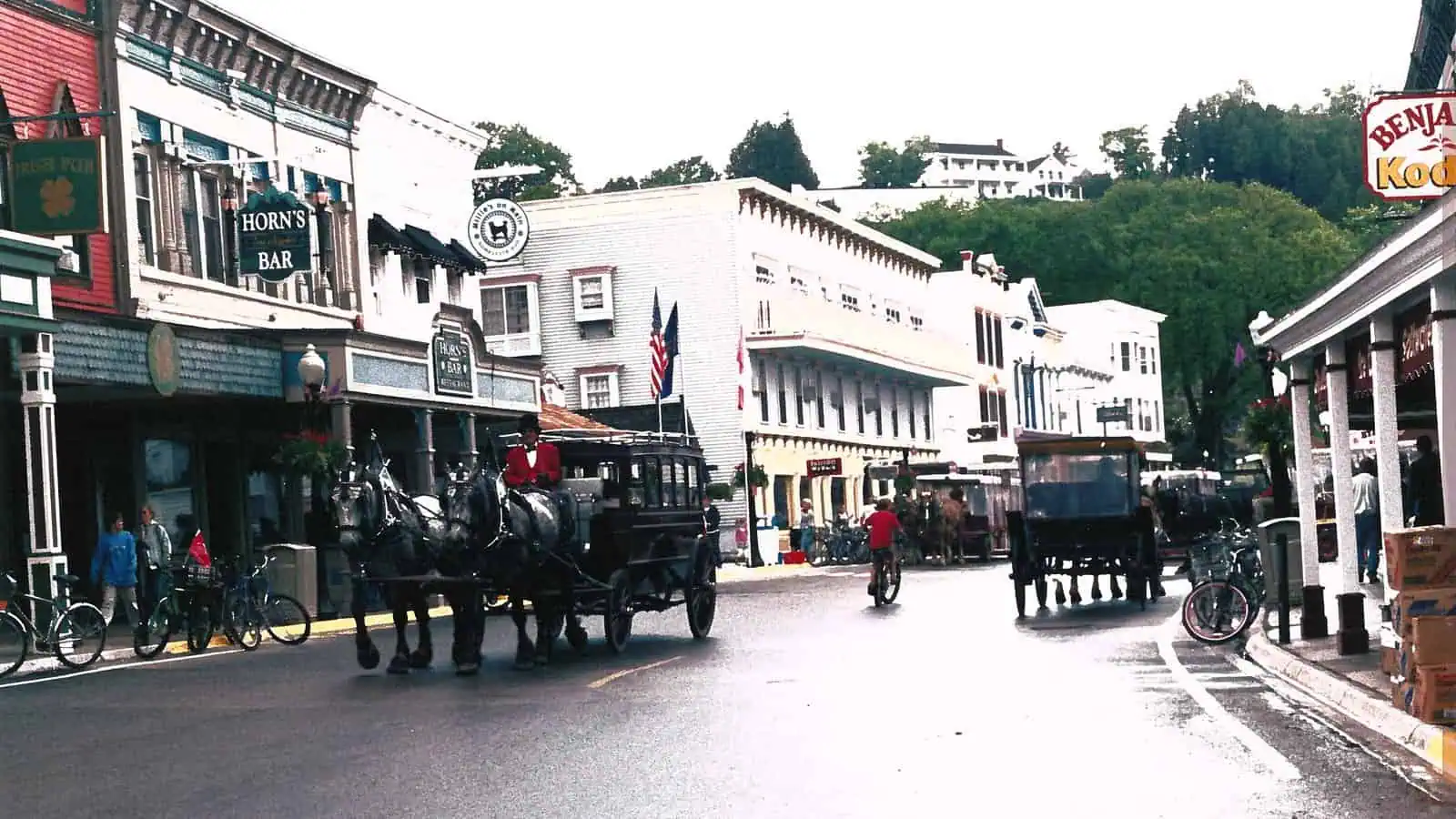 Horse-drawn carriages, a cyclist and racks of parked bicycles on Main Street, Mackinac Island.