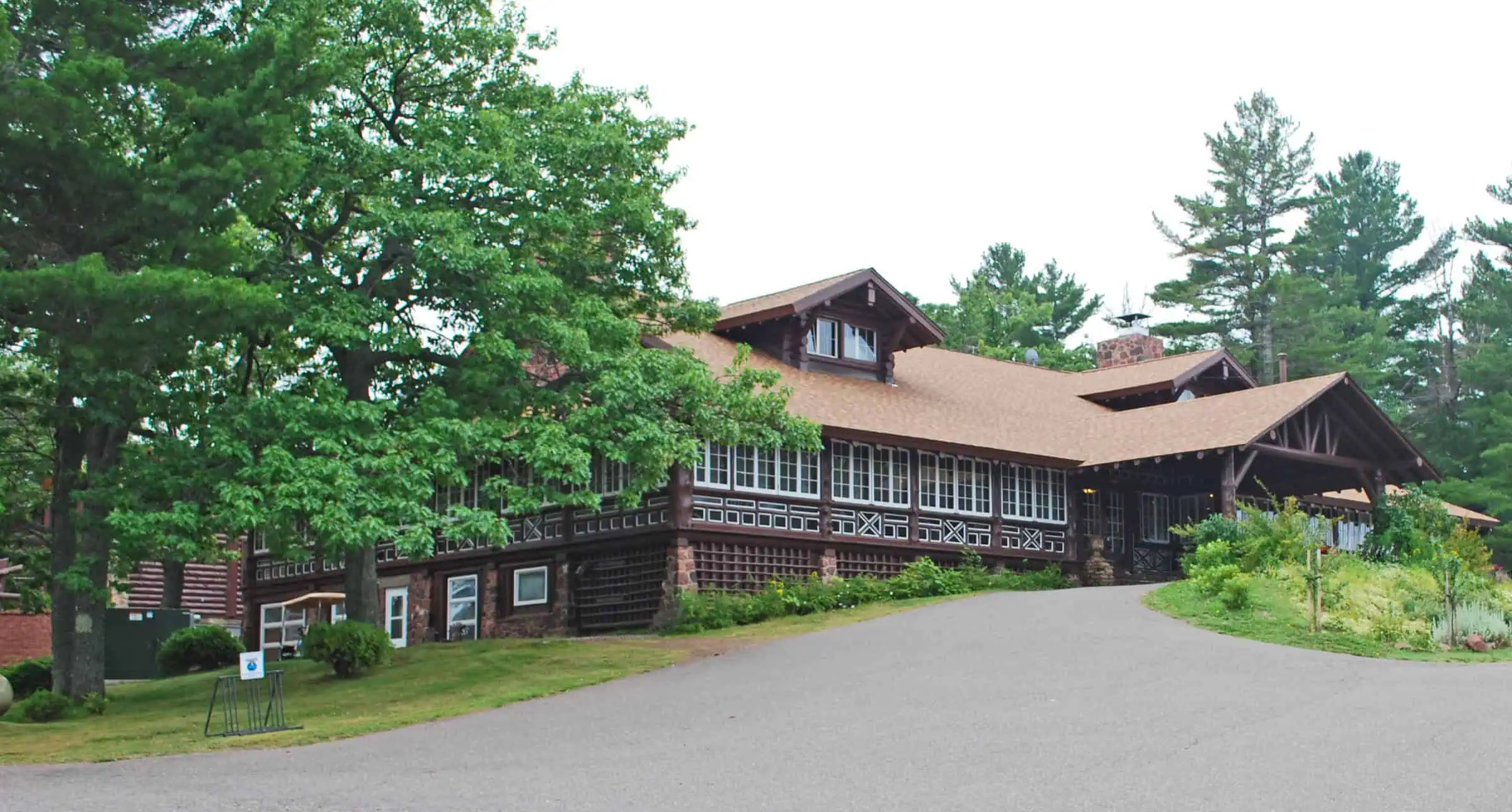 The dark log main building of Keweenaw Mountain Lodge with a low gabled roof, set among pines at the end of a paved drive near Copper Harbor. Photo: Andrew Jameson / Wikimedia Commons (CC BY-SA 3.0).
