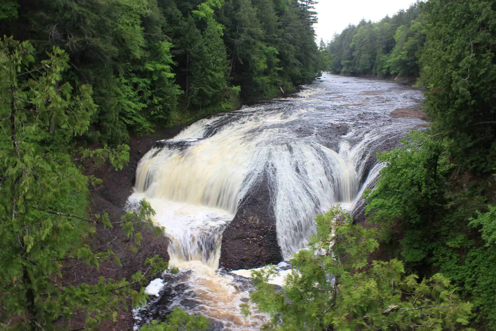 Potawatomi Falls, a wide tannin-brown waterfall pouring over dark rock between forested banks on the Black River. Photo: USDA Forest Service Eastern Region / Wikimedia Commons (Public domain).