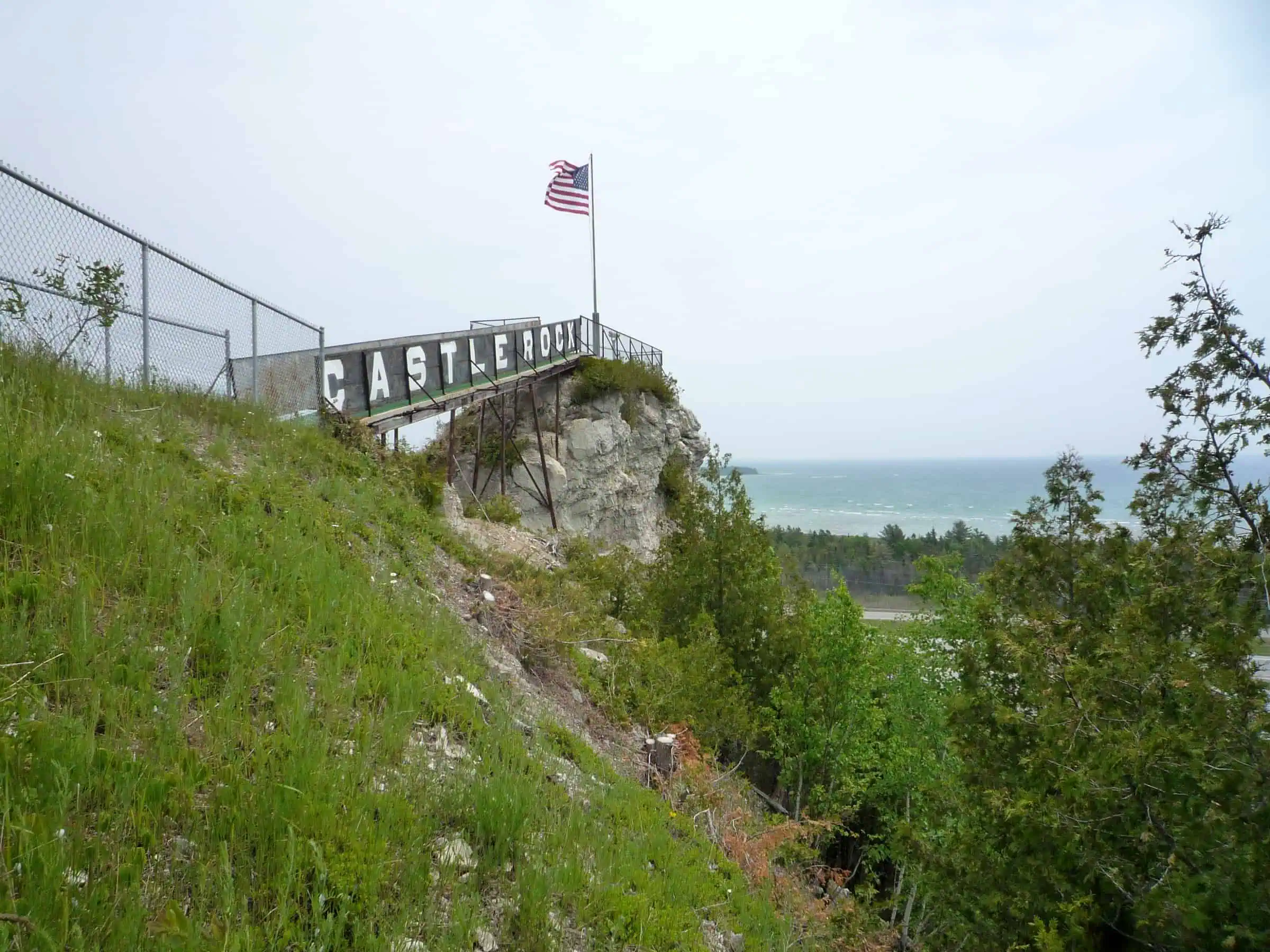 A grassy, tree-covered rock face rising to a fenced wooden viewing platform with an American flag, water visible beyond. Photo: Bobak Ha'Eri / Wikimedia Commons (CC BY 3.0).