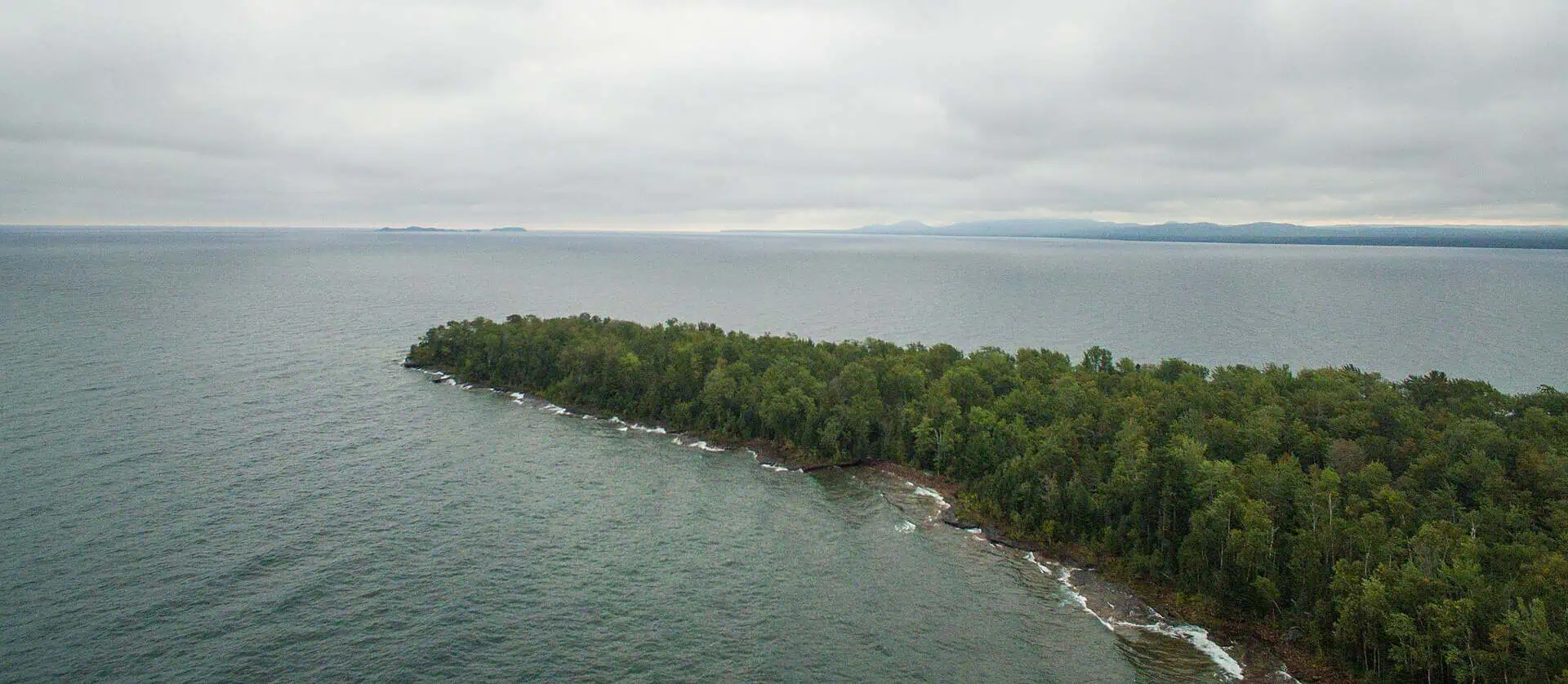 Rocky point of land on Lake Superior with forested hills on the horizon, Point Abbaye, Baraga County. Photo: RomanKahler, CC BY-SA 4.0.