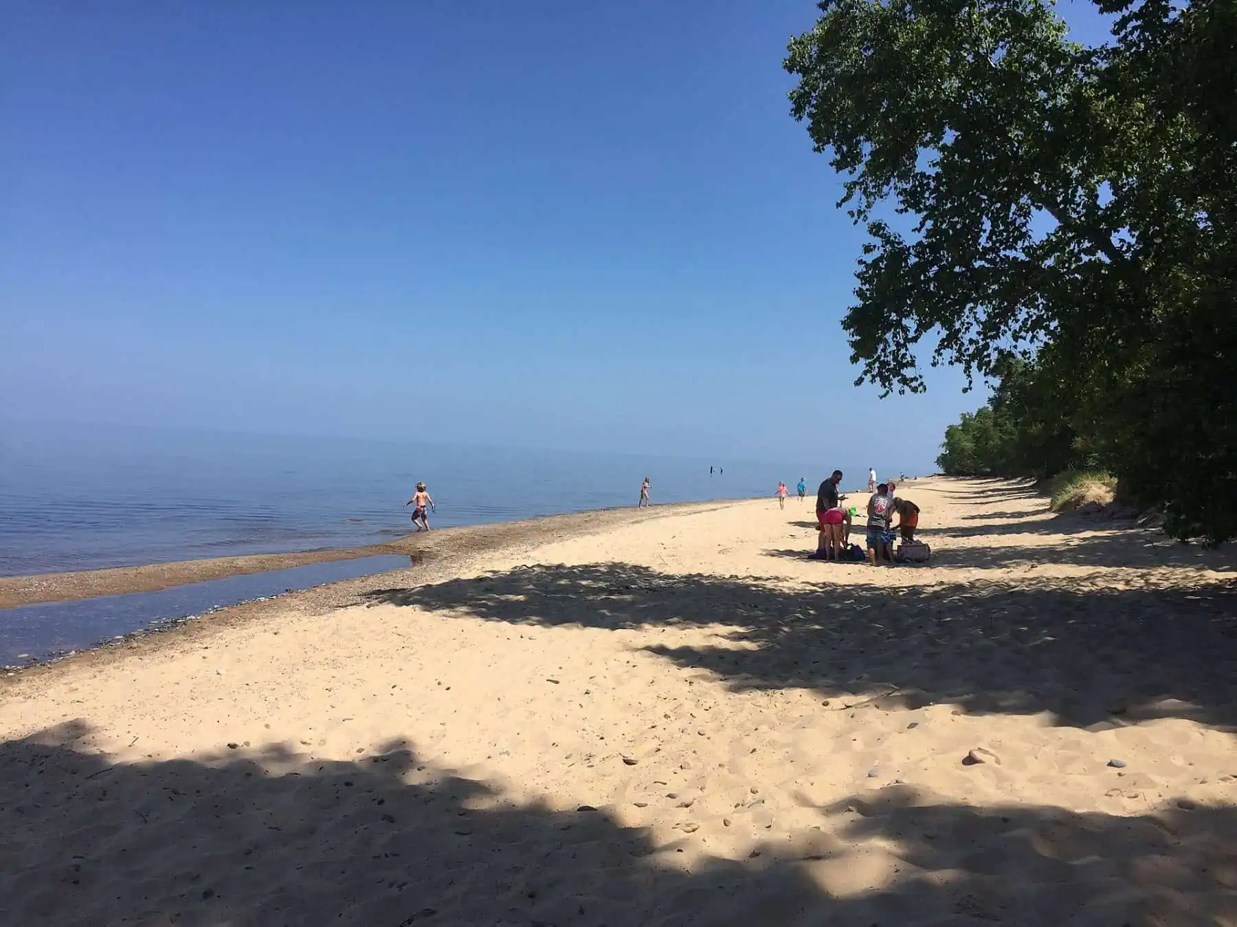 People wading and walking on the sandy beach at Hurricane River on Lake Superior on a sunny summer day. Photo: National Park Service, public domain.