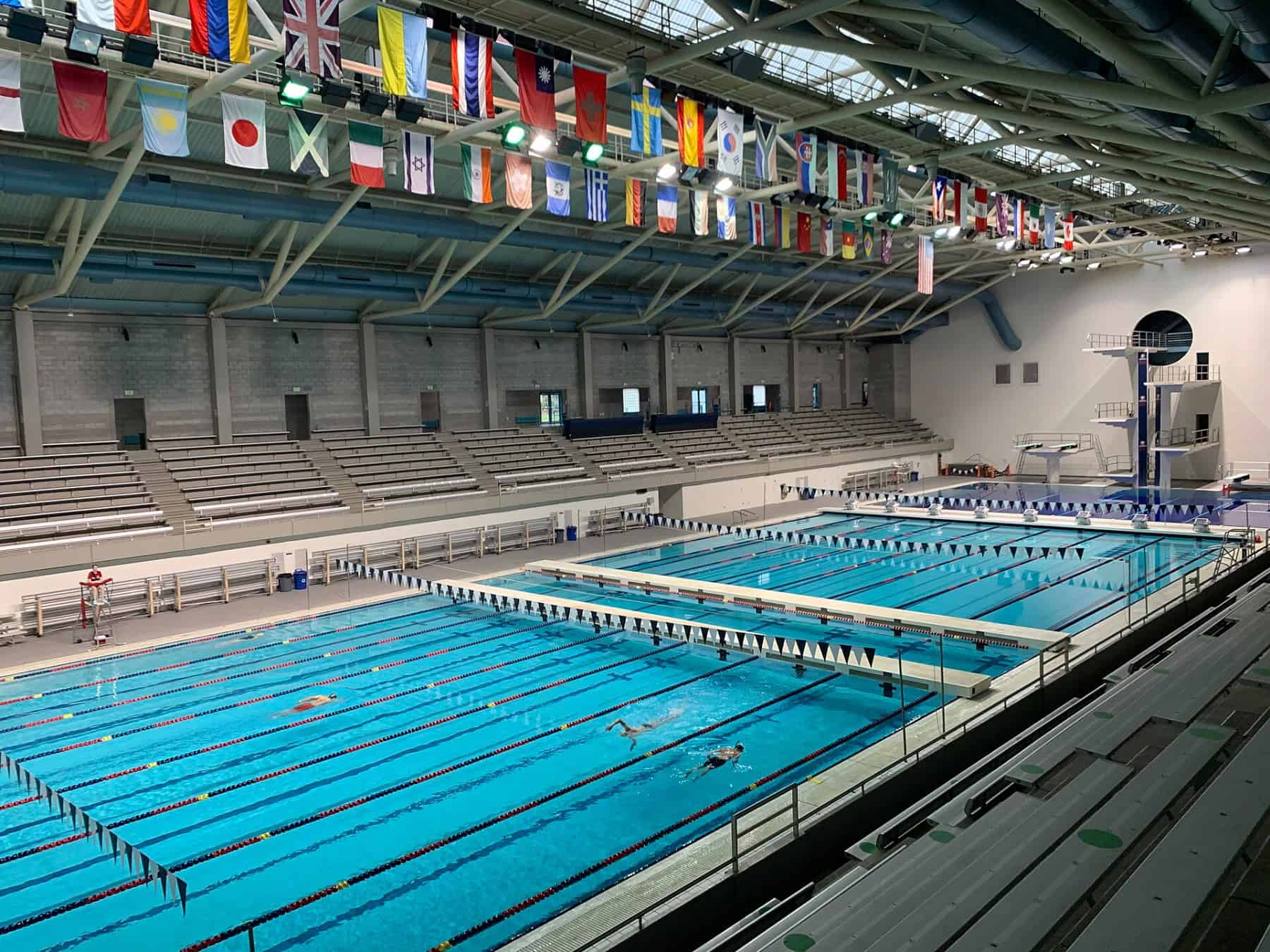 An Olympic-size indoor competition pool with lane lines, a diving tower and bleachers. Photo: Tanis Coralee Leonhardi, CC BY-SA 4.0.