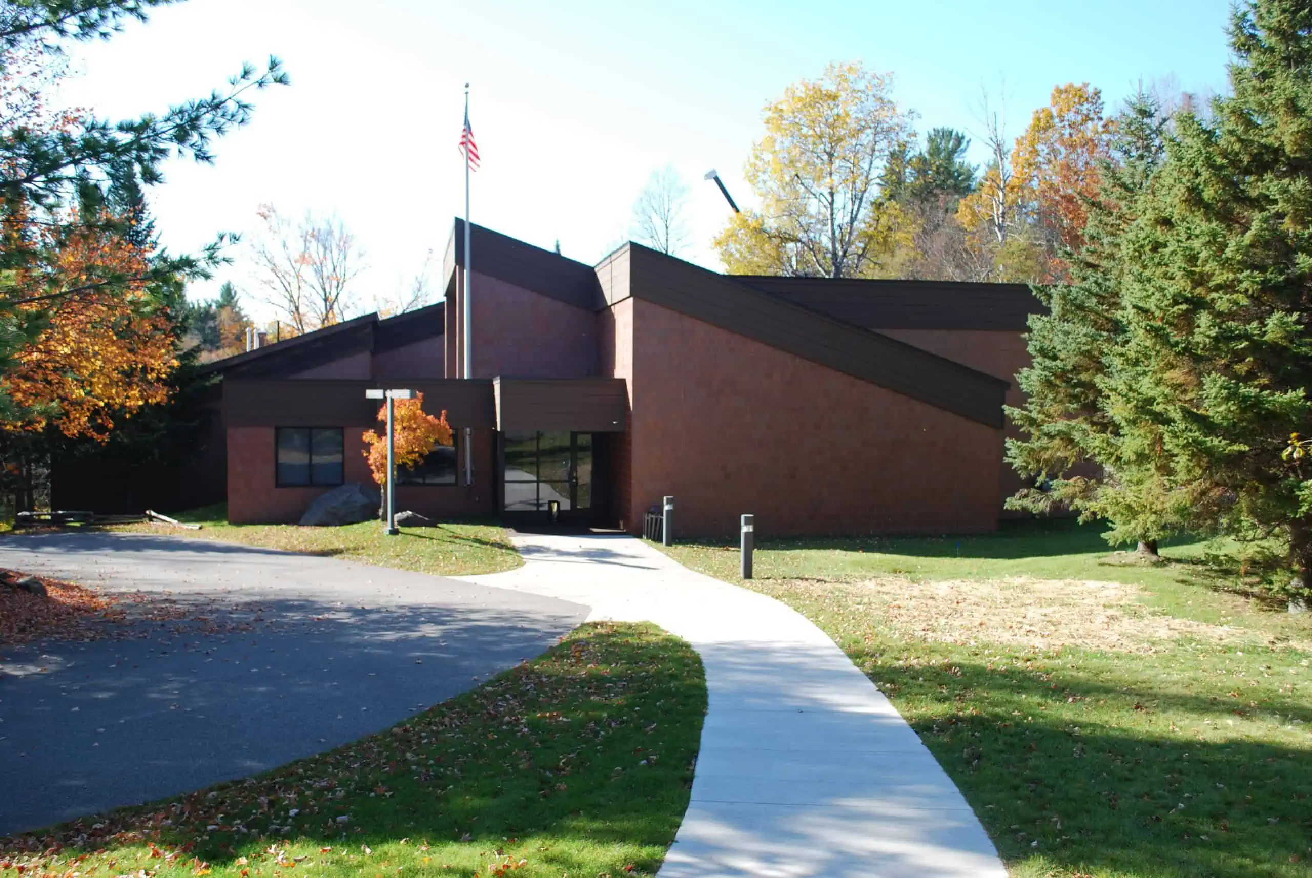 The Michigan Iron Industry Museum, a low brown building with a flagpole, a curving walkway and fall color behind it. Photo: Andrew Jameson / Wikimedia Commons (CC BY-SA 4.0).